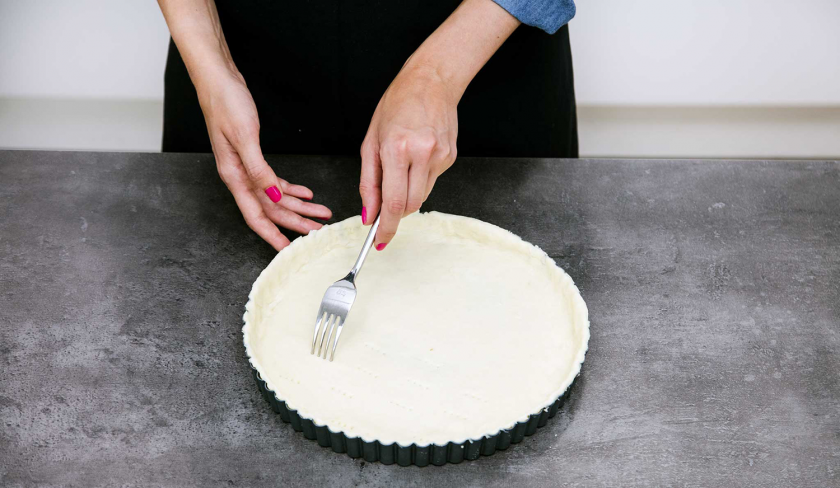 Der Boden der Spinat-Quiche wird mit einer Gabel eingestochen.