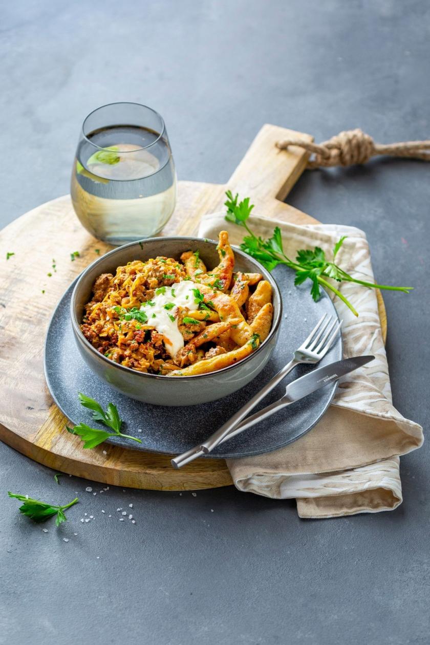 Spitzkohl mit Hackfleisch und Schupfnudeln in einer Schale mit angelegtem Besteck.