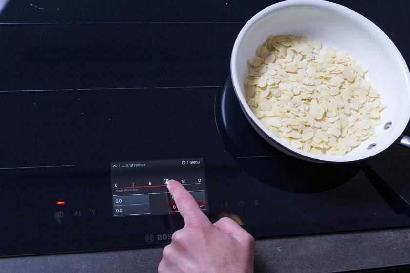 Mandelblättchen in einer Pfanne auf dem Herd, der eingeschaltet wird.