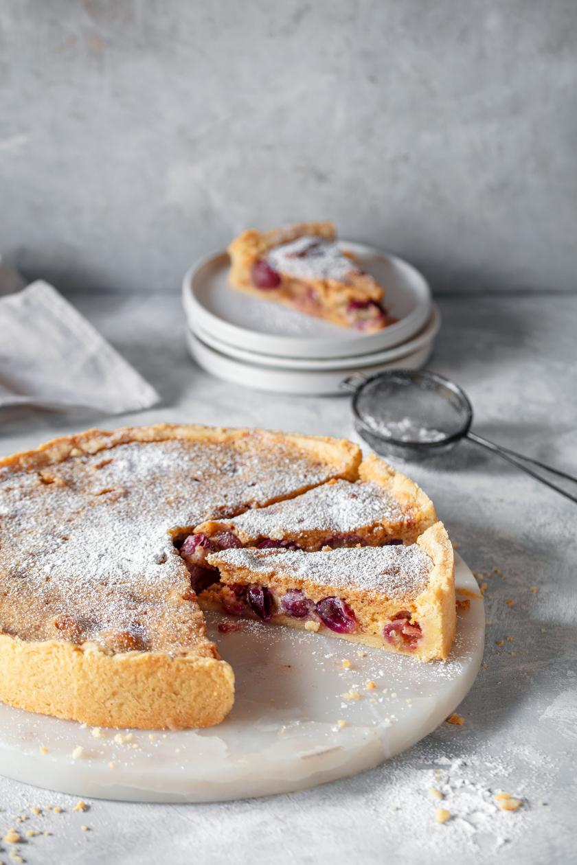 Traubenkuchen mit Mandelguss angeschnitten auf einer Kuchenplatte.