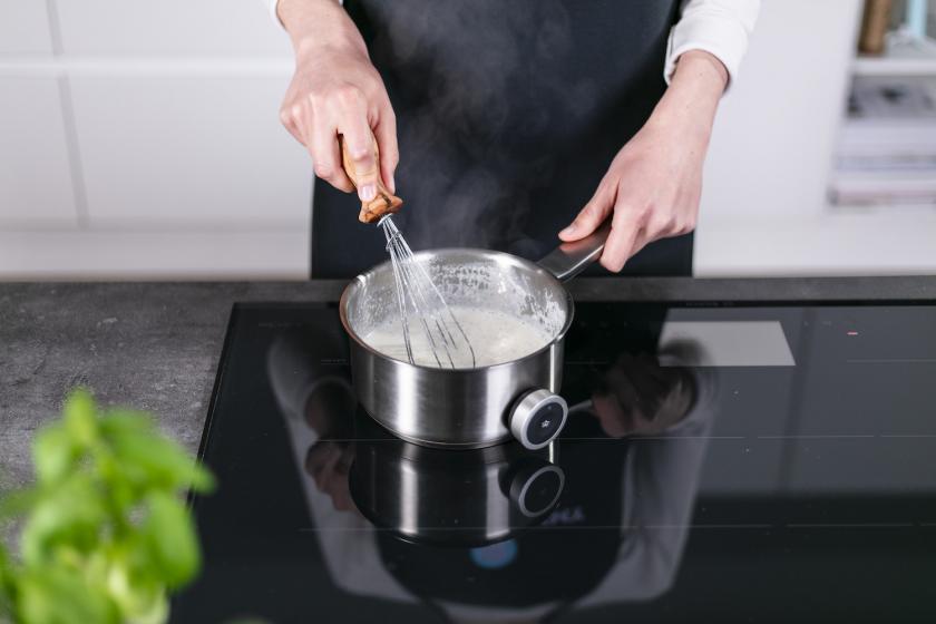 Milch wird in einem Topf aufgekocht und mit einem Schneebesen verrührt.