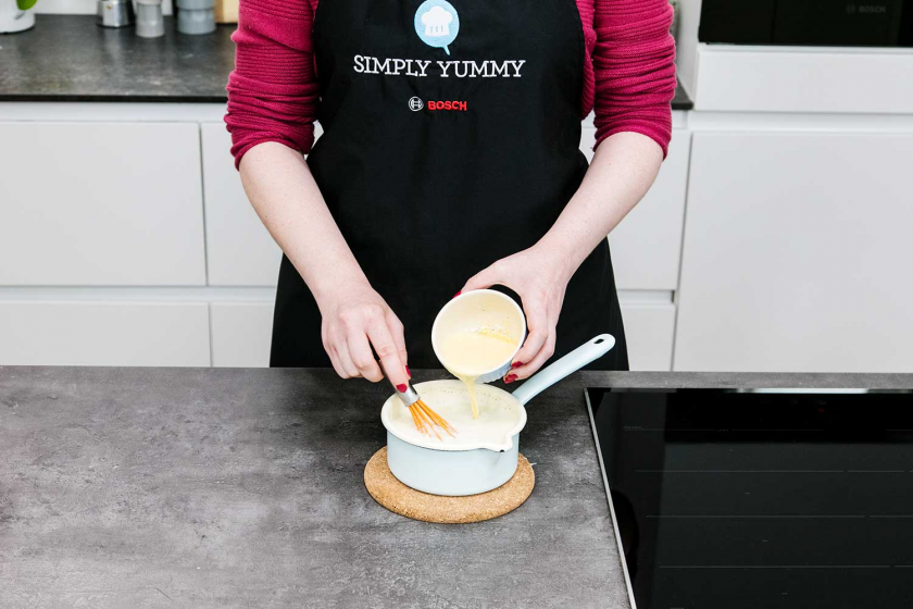 Eigelb wird in die Milchmischung für die Vanillesoße gegeben.