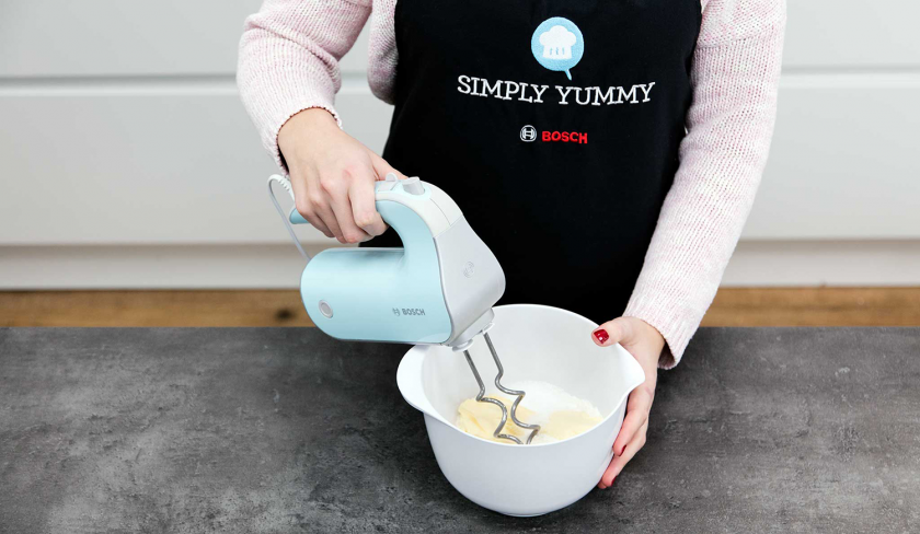 Die Zutaten für den Boden des veganen Käsekuchens werden in einer Schüssel mit einem Handmixer verknetet.