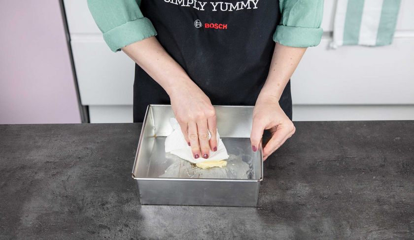 Für weiße Schoko-Kokos-Blondies wird eine Backform eingefettet.