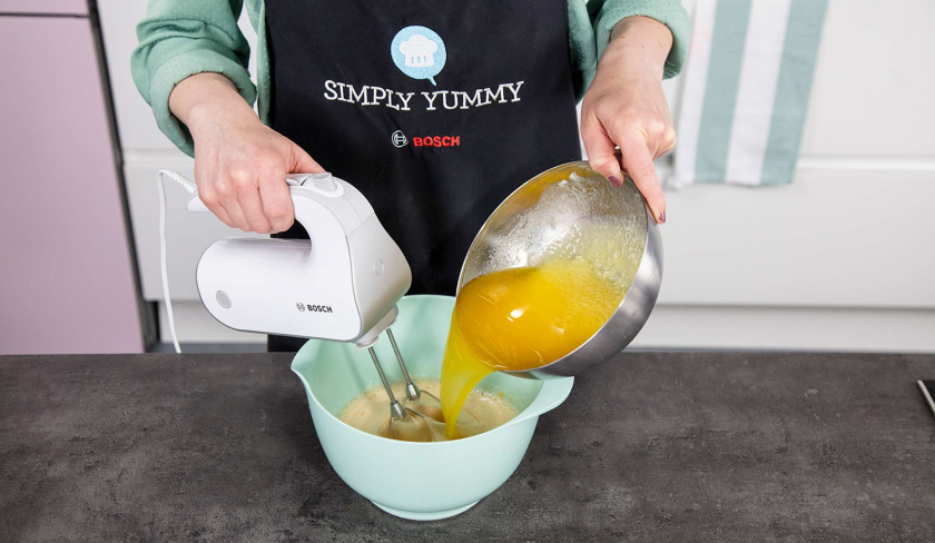 Für weiße Schoko-Kokos-Blondies werden die flüssigen Zutaten in einer Schüssel mit einem Handmixer verrührt.