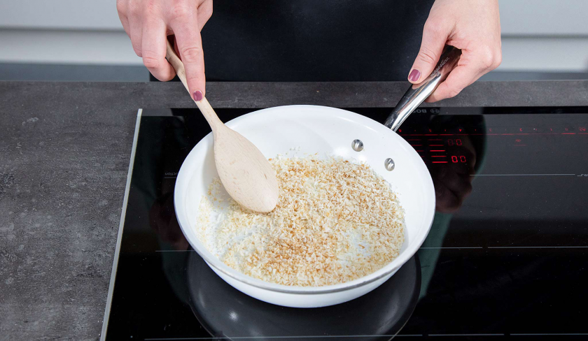 Für weiße Schoko-Kokos-Blondies werden Kokosflocken in einer Pfanne geröstet.
