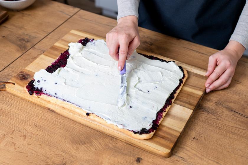 Creme wird auf die Biskuitplatte für die Wickeltorte gestrichen.