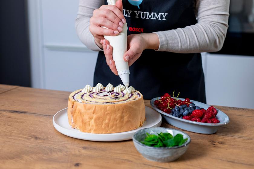 Wickeltorte wird mit Cremetupfen dekoriert.