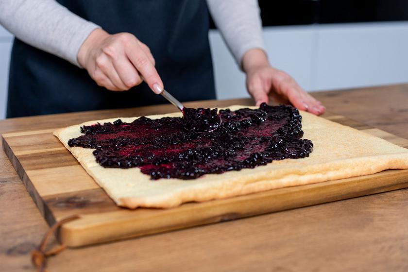 Blaubeerkompott wird auf die Biskuitplatte für die Wickeltorte gestrichen.