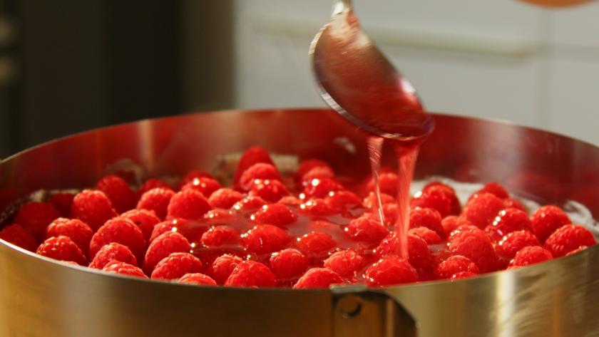 Tortenguss wird über der Windbeuteltorte mit Himbeeren verteilt.