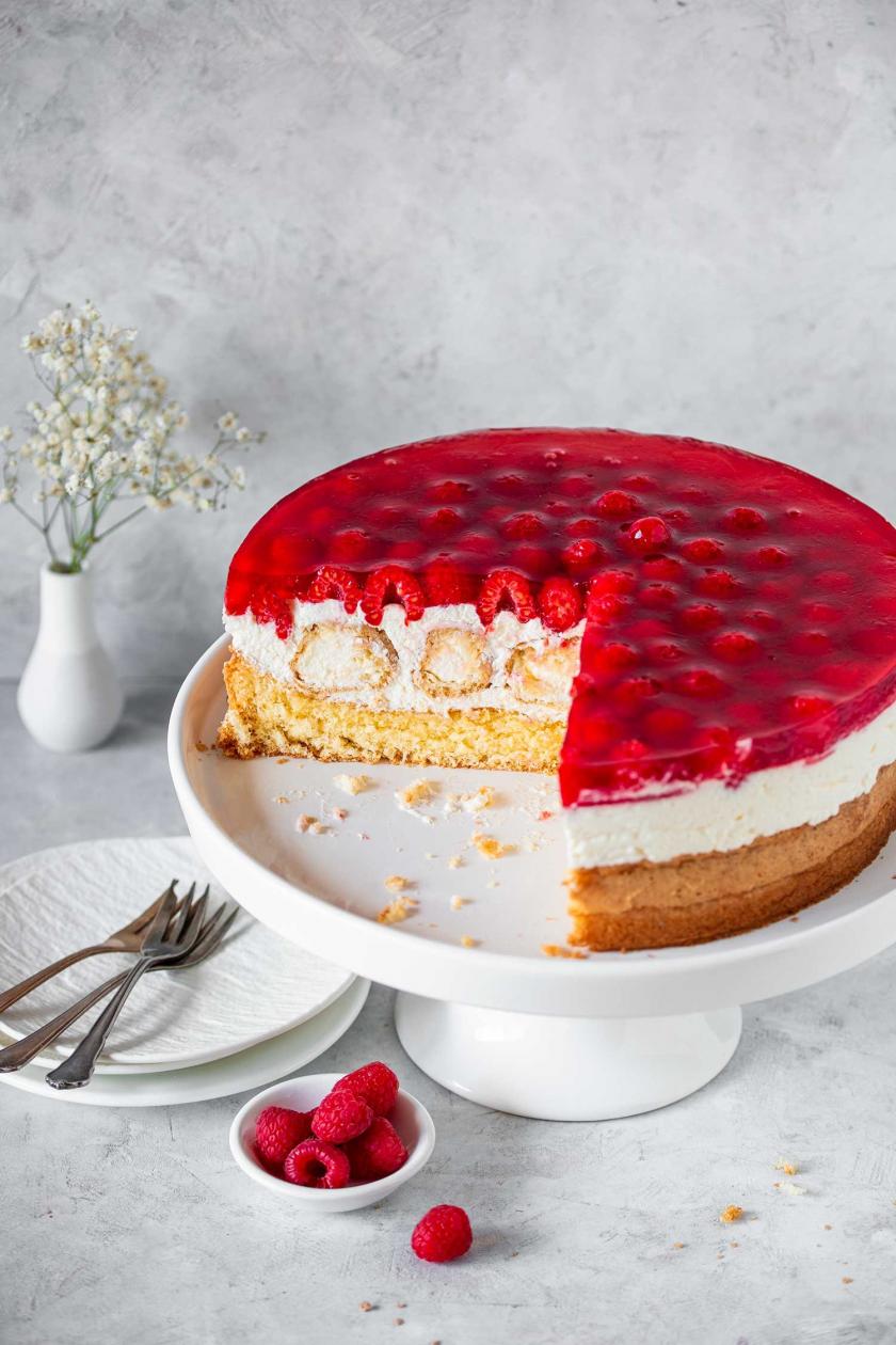 Windbeuteltorte mit Himbeeren angeschnitten auf einer Kuchenplatte.