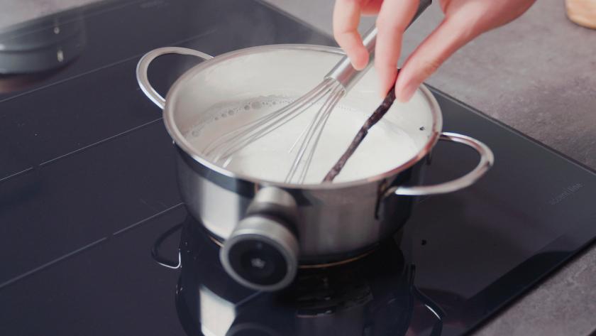 Vanilleschote wird aus einem Topf mit Milch entfernt.