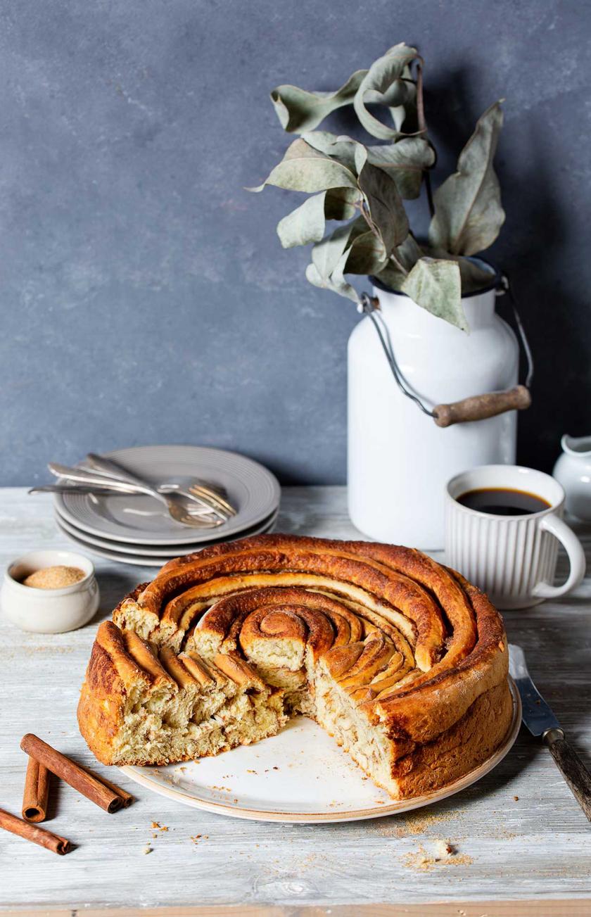 Zimtrolle angeschnitten auf einem gedeckten Kaffeetisch.