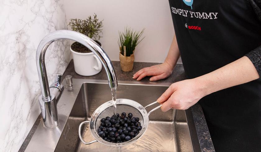 Für die Zitronen-Blaubeermuffins mit Streuseln werden Blaubeeren in einem Sieb unter fließendem Wasser gewaschen.