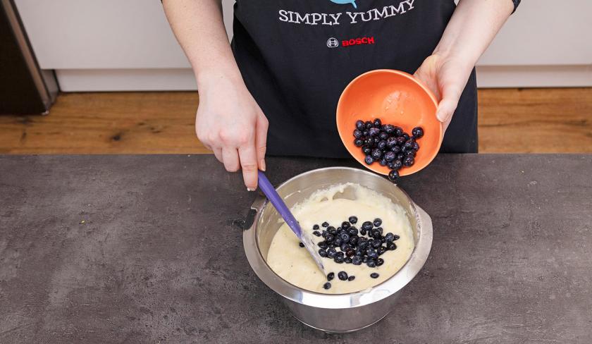 Blaubeeren werden unter den Teig für die Zitronen-Blaubeermuffins mit Streuseln gehoben.