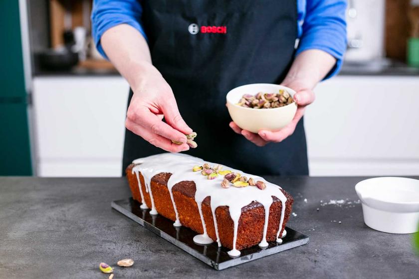Pistazien werden auf der Glasur des Zitronenkuchens mit Frischkäse verteilt.