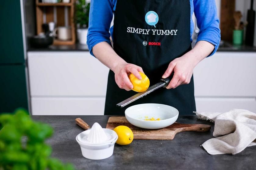 Zitronenschale wird über einem Teller abgerieben.