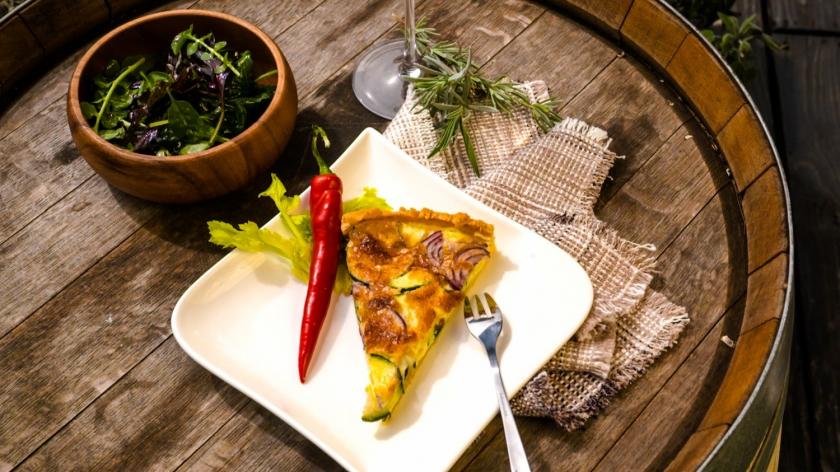 Ein Stück Zucchini-Quiche mit Salat und Chili auf einem Teller.