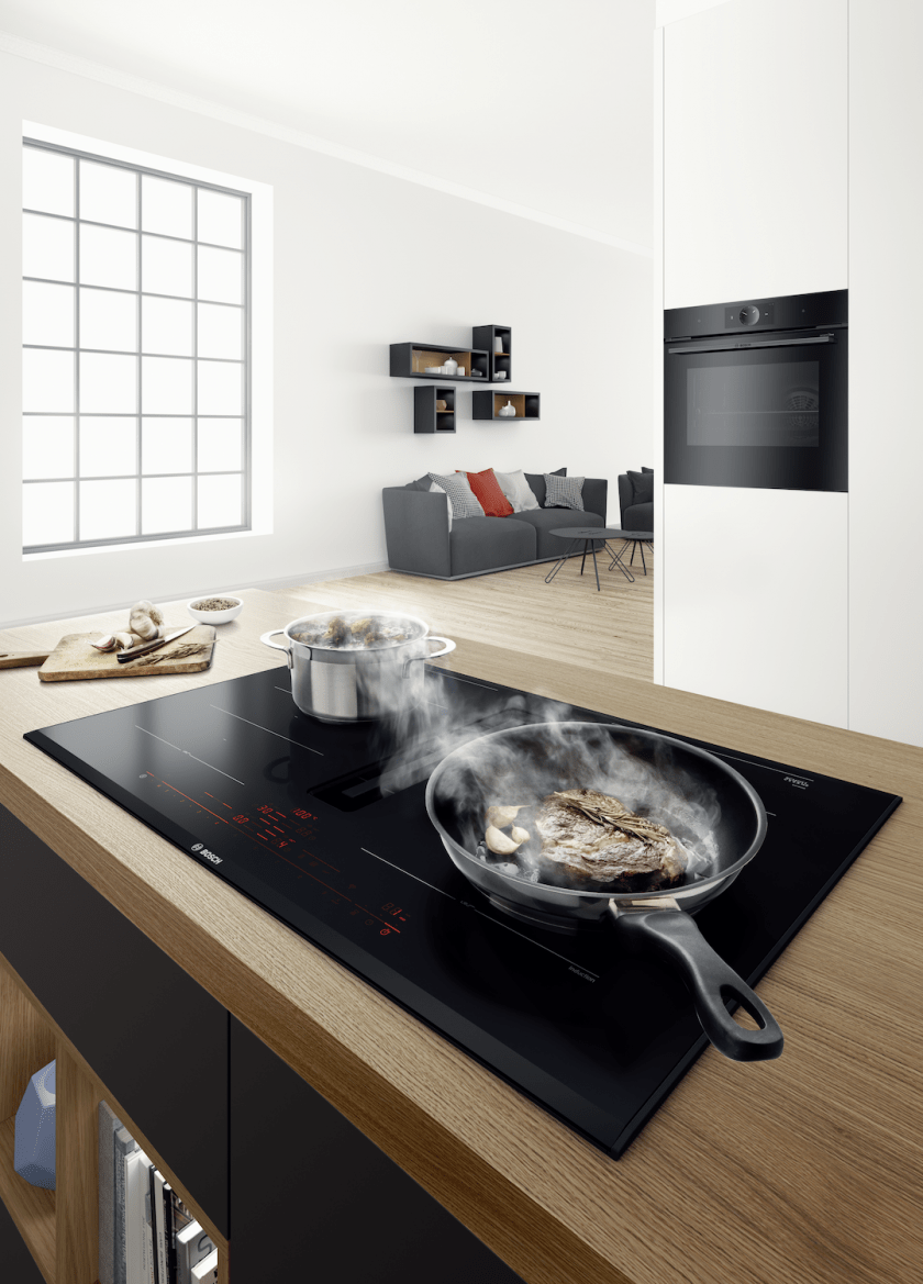 Induktuonskochfeld auf dem eine Pfanne und ein Topf steht. Im Hintergrund ist eine Wohnung zu erkennen.