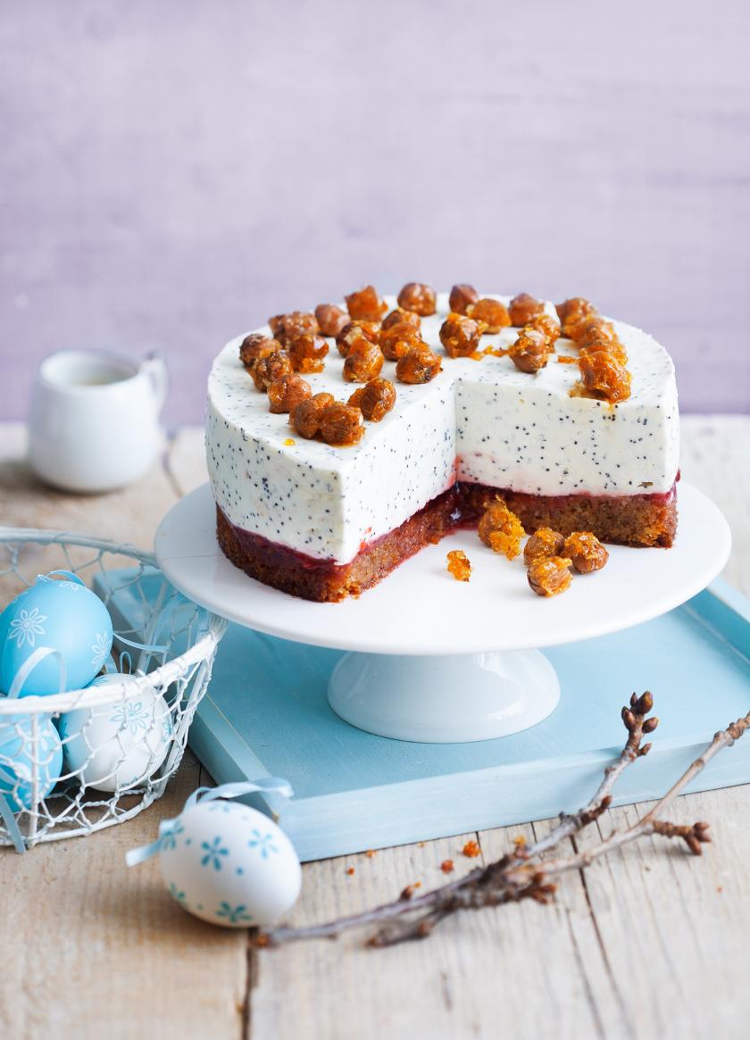 Joghurttorte angeschnitten auf einer Tortenplatte auf einem Holztisch, daneben Ostereier