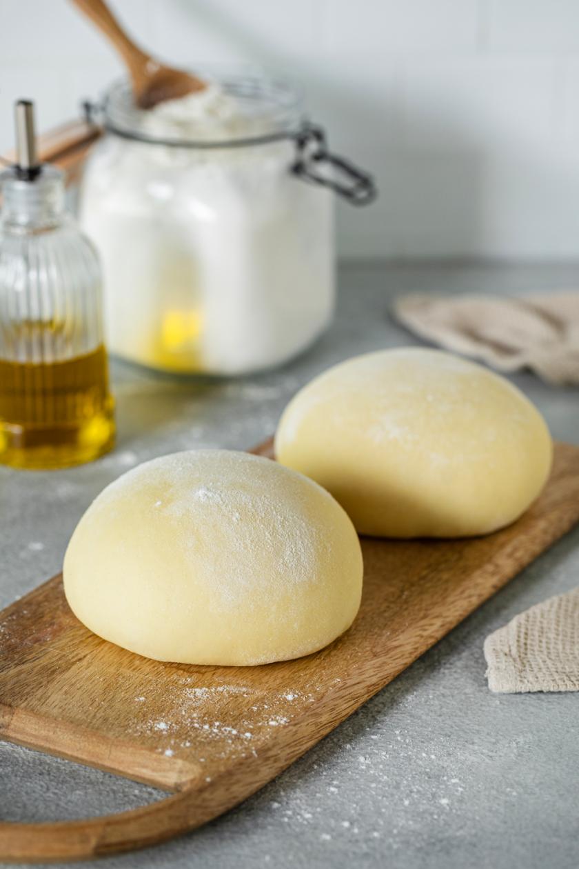 Zwei Pizzateigkugeln auf einem Holzbrett