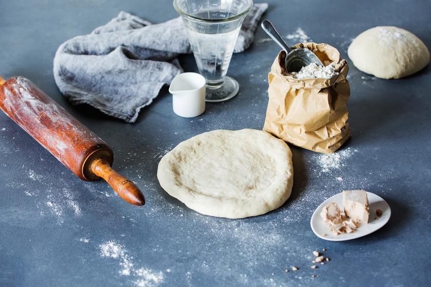 Pizzateig rund ausgerollt auf einer Arbeitsplatte, daneben Mehl