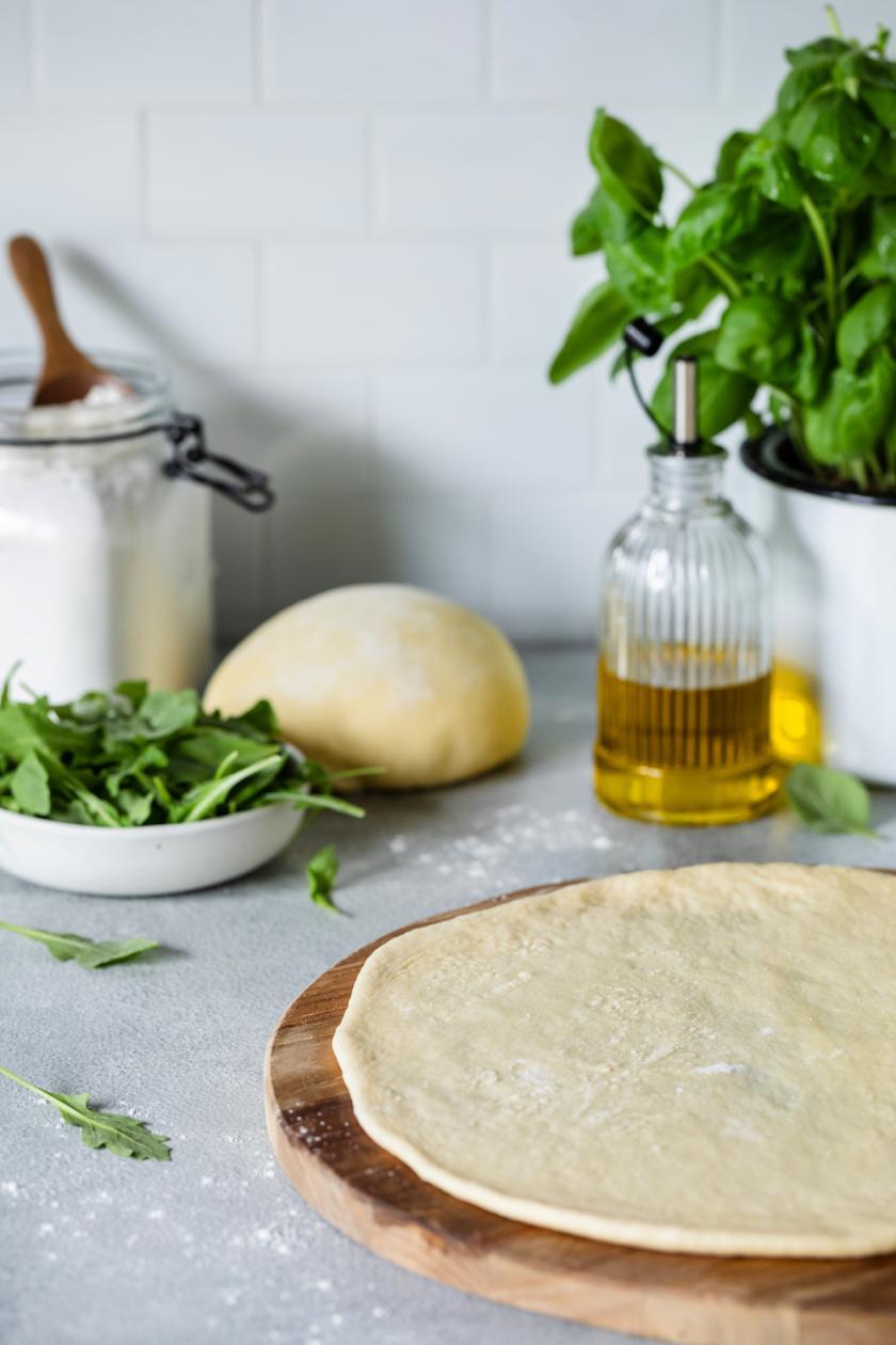 Glutenfreier Pizzateig ausgerollt auf einem runden Holzbrett