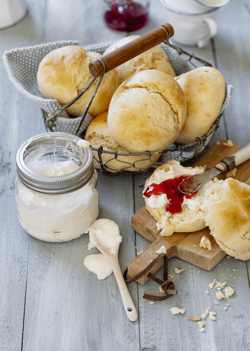 Brötchenmix in einem Brotkorb aus Draht auf einem Tisch, daneben Marmelade und Quark